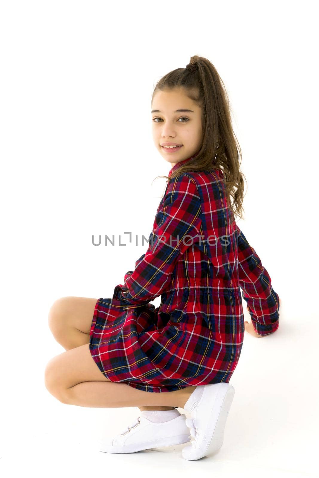 Beautiful little girl kneels in the studio on a white background. The concept of beauty and fashion, children's emotions. Isolated on a white background.