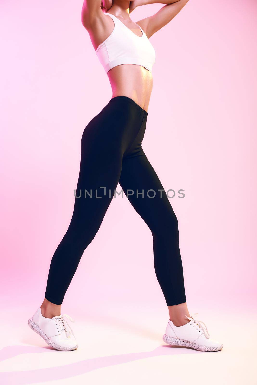 Perfect shape. Cropped photo of sporty slim woman in sportswear standing against pink background in studio. Sport. Active lifestyle. Studio shot