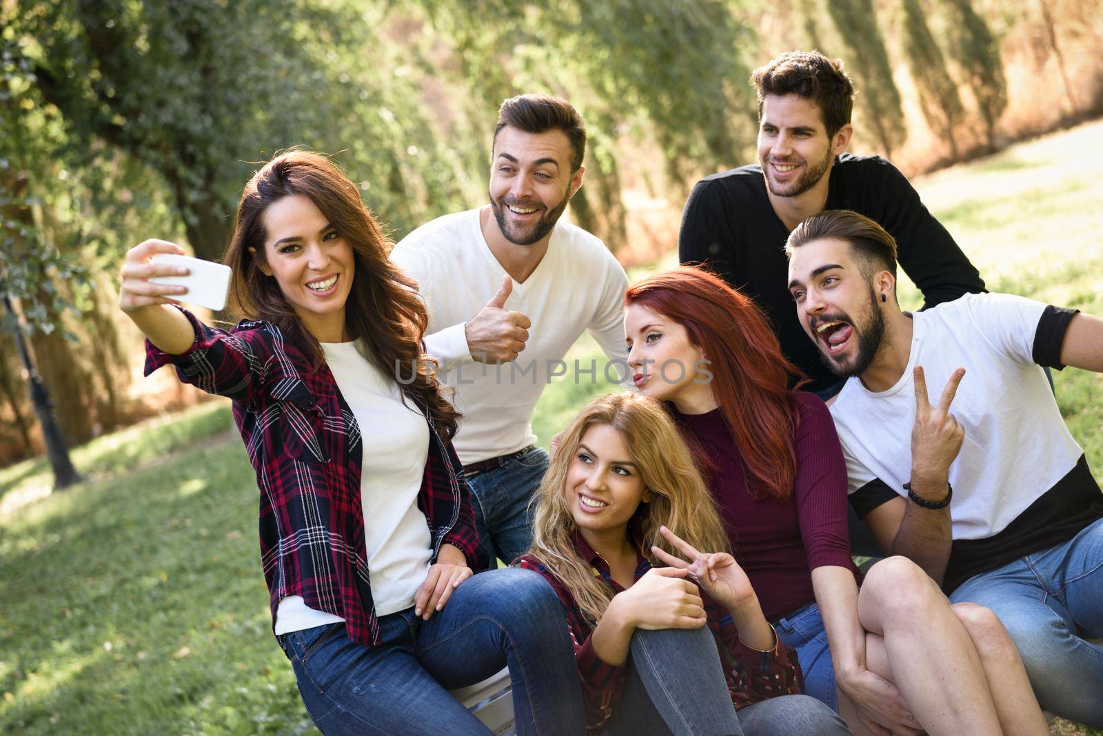 Group of friends taking selfie in urban park. Five young people wearing casual clothes.