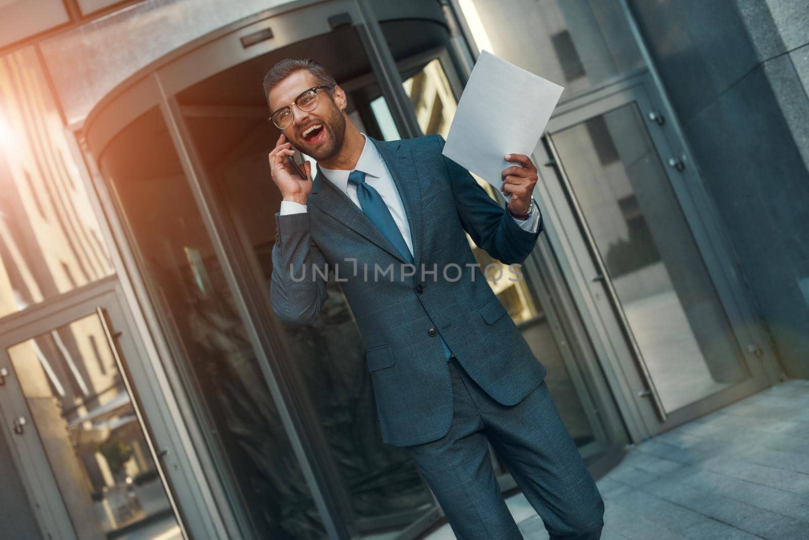 Great news Portrait of happy bearded businessman in full suit talking by phone with client and smiling while walking outdoors by friendsstock