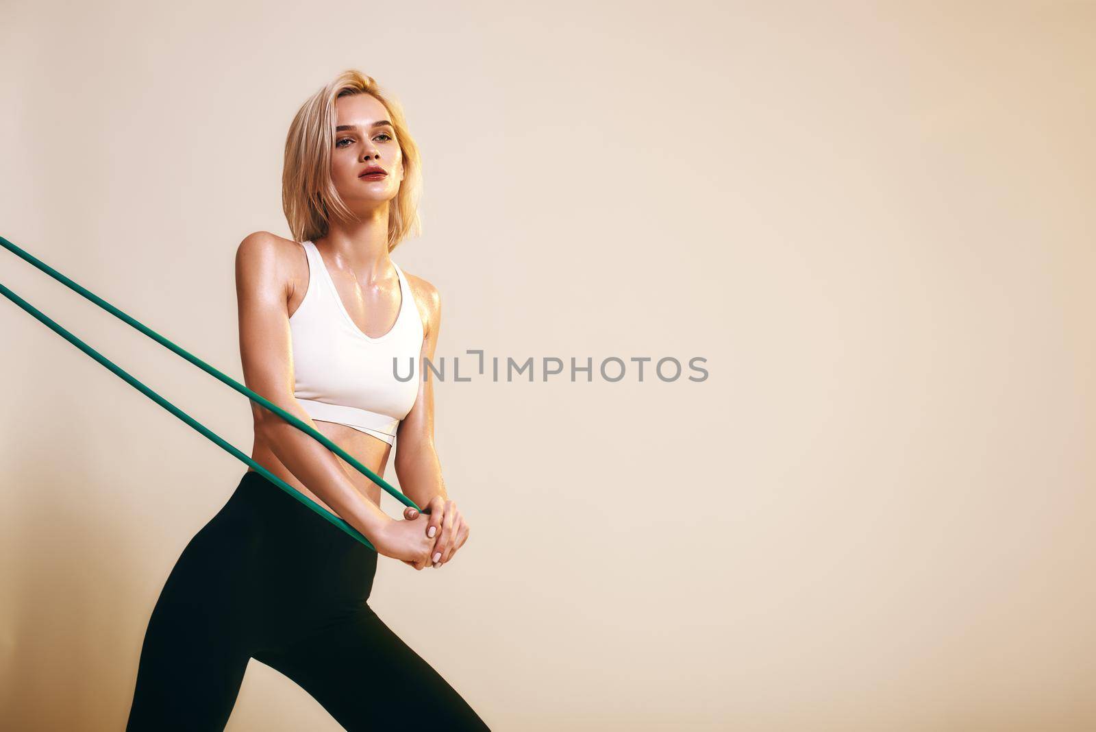 Flexibility. Sporty young woman in white top and black leggings working out with elastic band while standing in studio by friendsstock