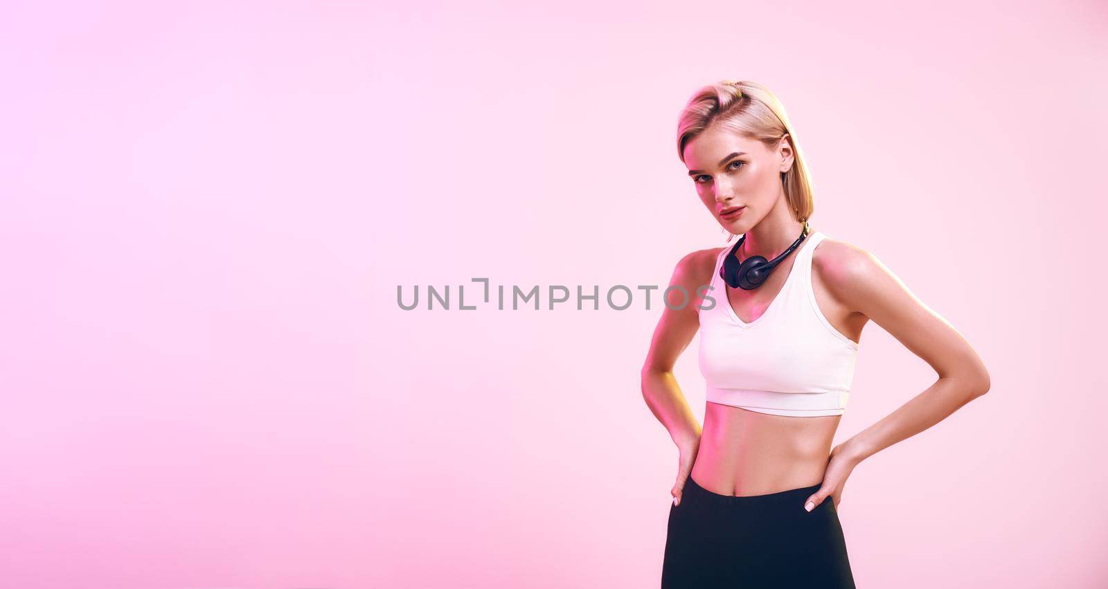 Music for workout. Beautiful and sporty woman in headphones looking at camera while standing against pink background. Web banner by friendsstock