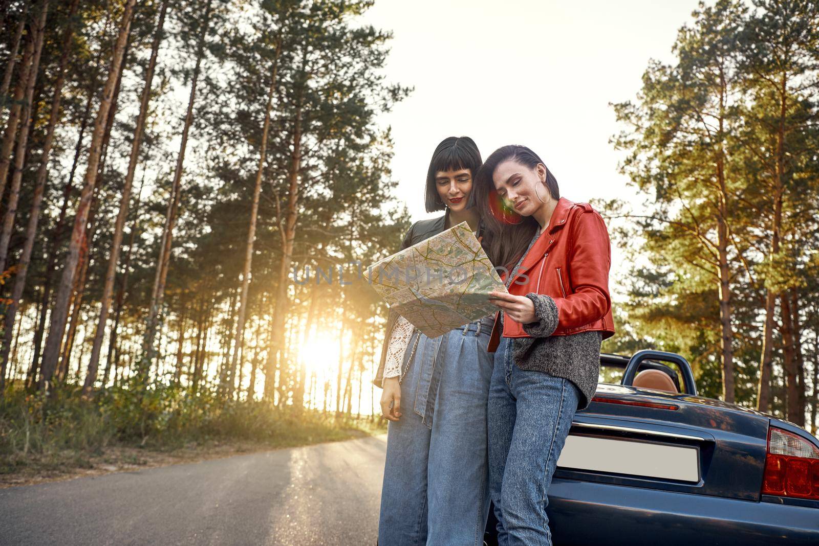 Two women trying to find the way on map near cabriolet by friendsstock