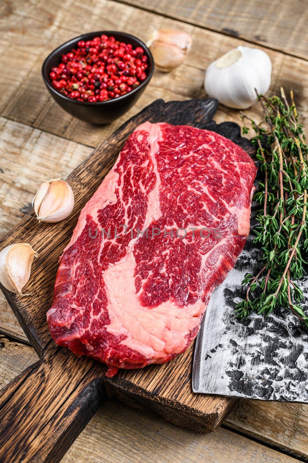 Prime rib eye raw beef meat steak on a butcher wooden cutting board with cleaver. wooden background. Top view.