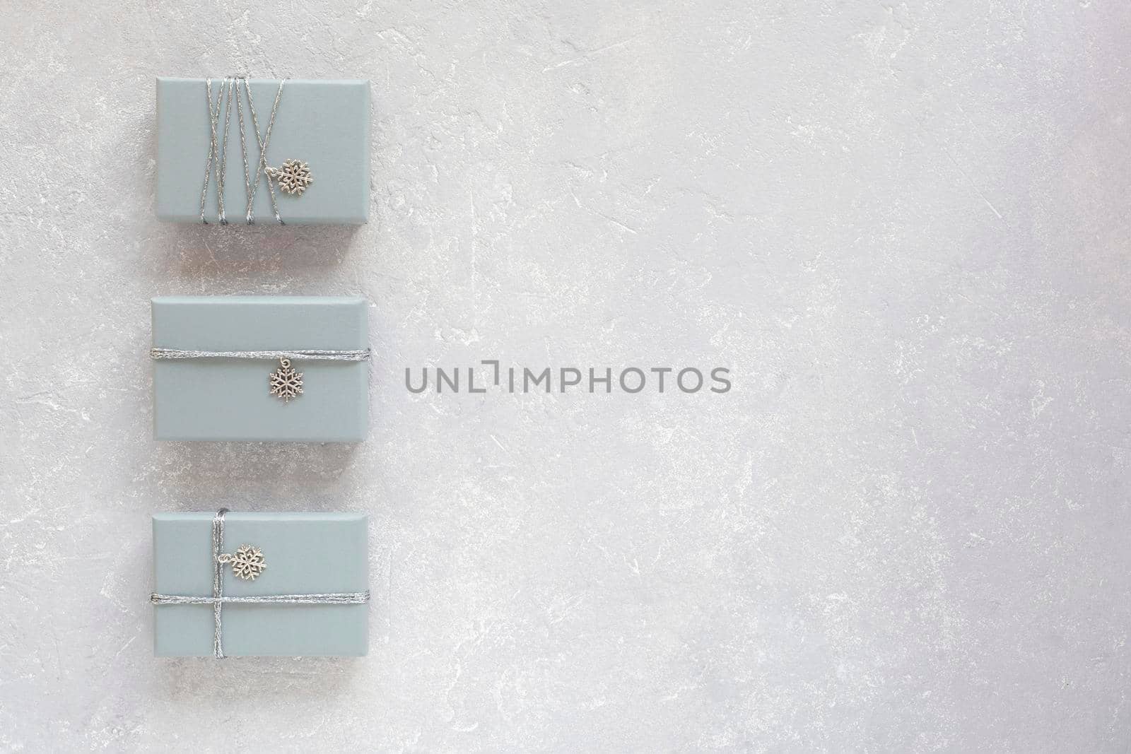 three grey gift boxes decorated with silver ribbon and snowflake pendant, on grey background, top view, copy space