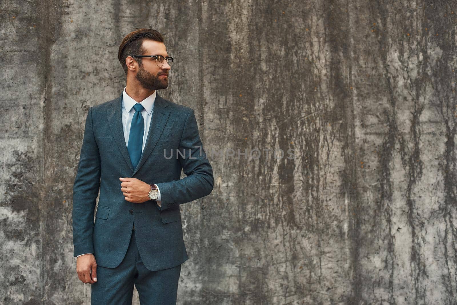 Great style. Confident bearded businessman in full suit looking away while standing against grey stone wall outdoors by friendsstock