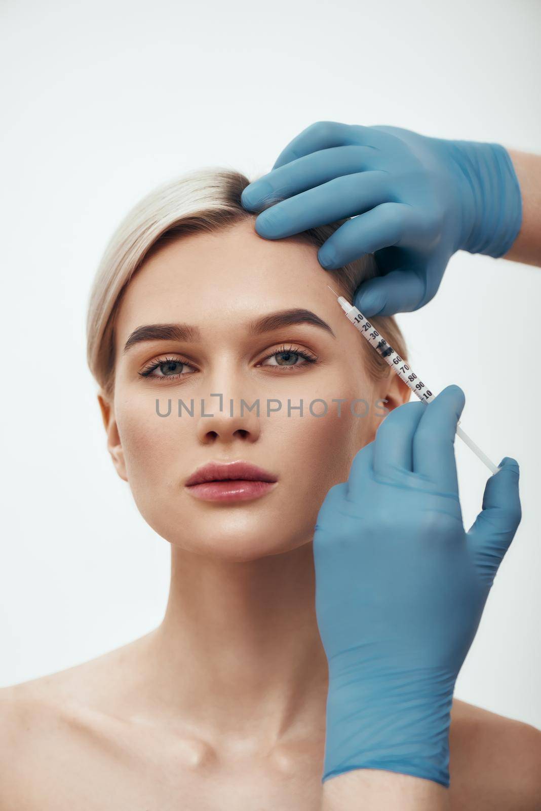 Say No to Wrinkles. Portrait of young pretty woman looking at camera while doctors hand in blue medical gloves making an injection in her face. Botox concept. Beauty. Facial surgery