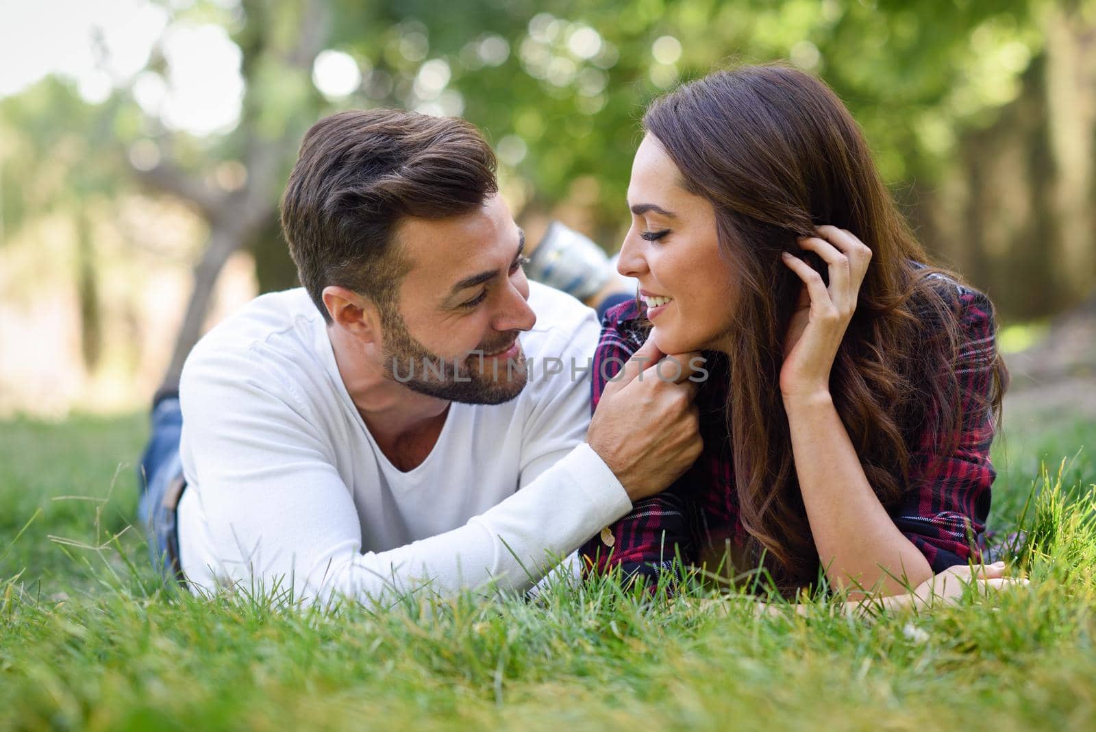 Beautiful young couple laying on grass in an urban park. Caucasian man and woman wearing casual clothes.