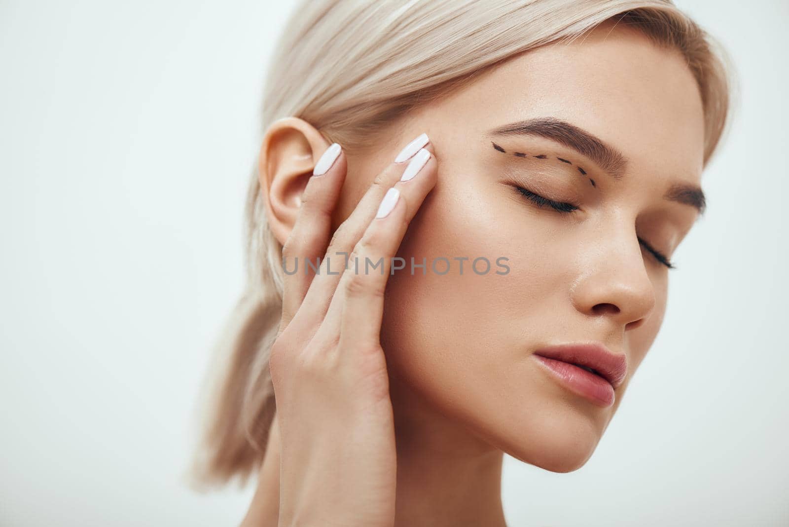 Plastic surgery. Beautiful young blonde woman keeping eyes closed and touching her face with sketch on it by friendsstock