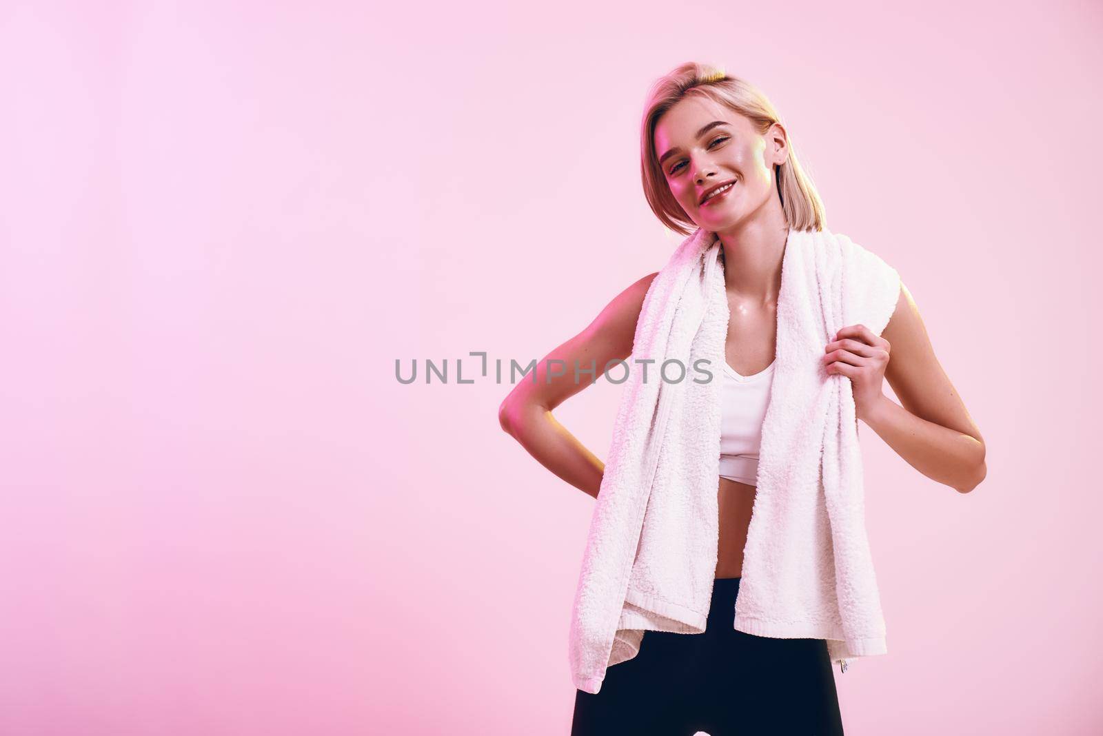 Healthy and happy. Positive and cute blonde woman with towel on shoulders looking at camera with smile while standing against pink background in studio by friendsstock