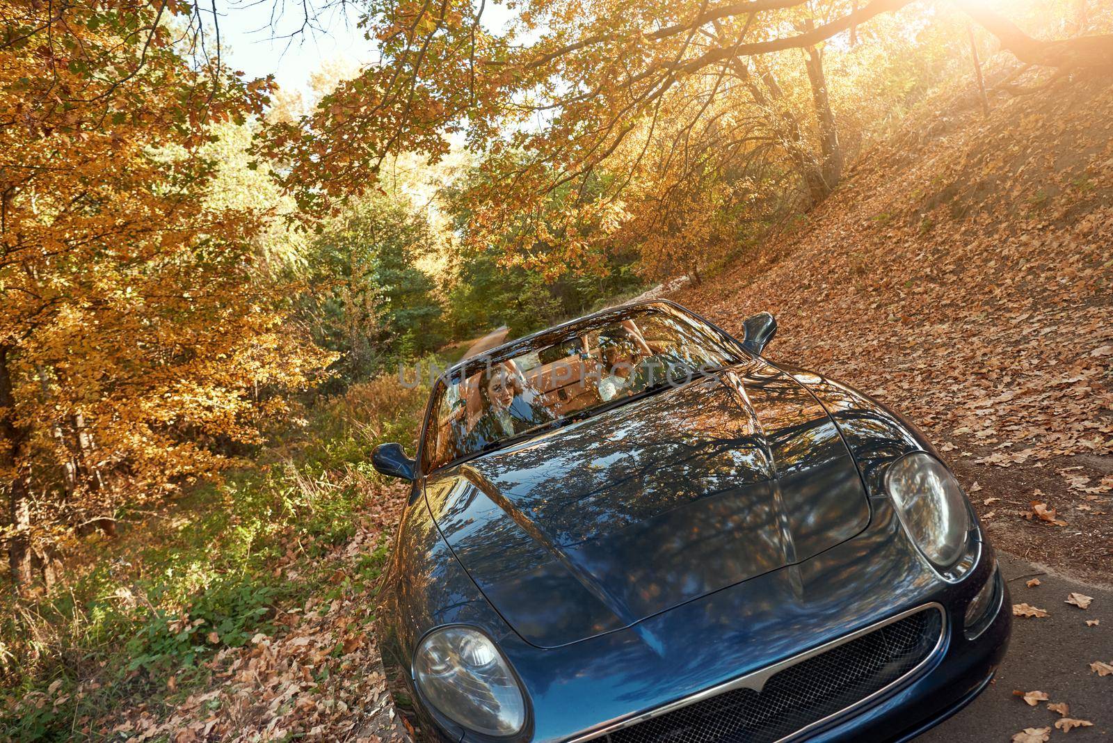 A black roofless car driving fast on the countryside asphalt road against morning sky with a beautiful sunrise. Autumn season, falling leaves