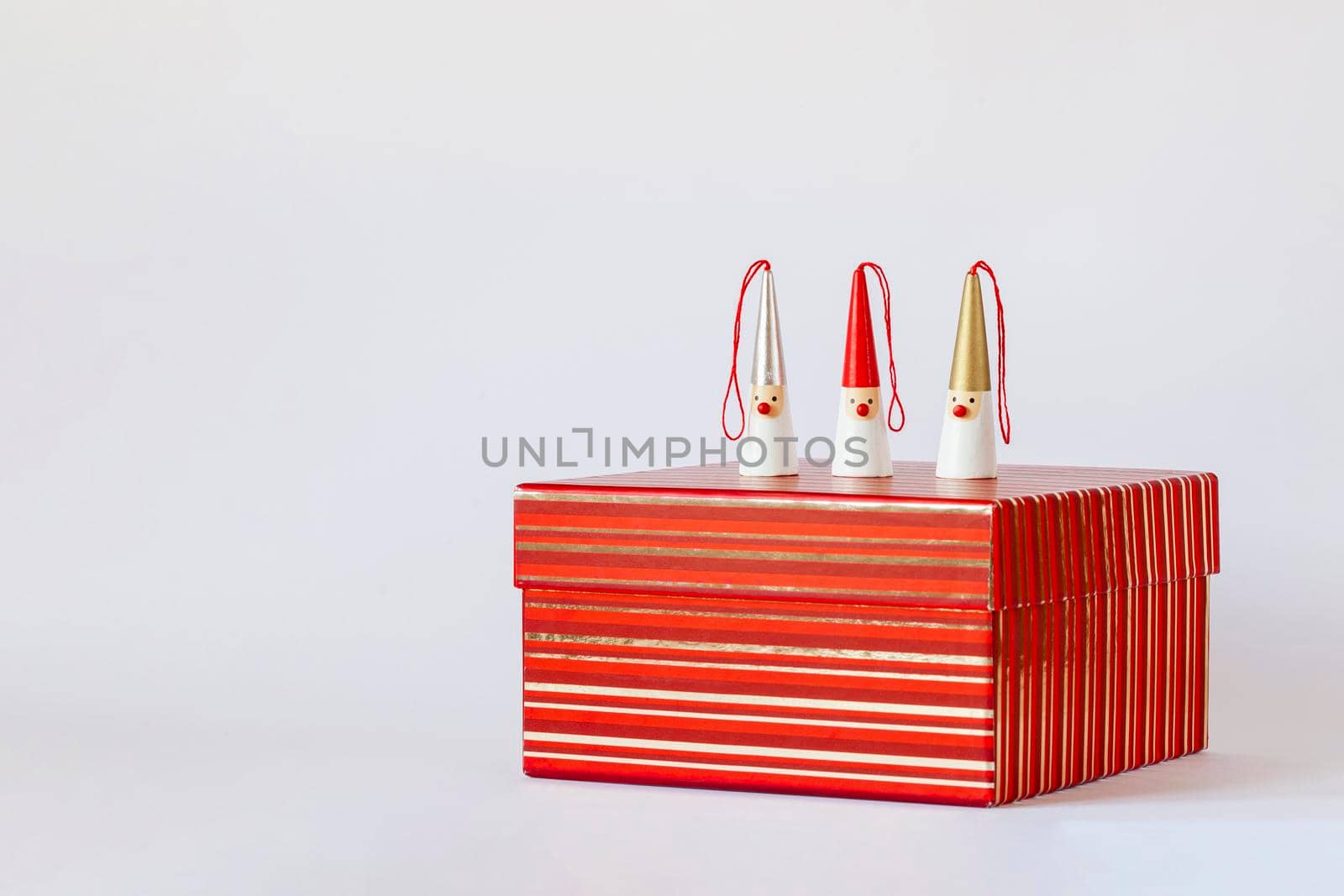 three Santa Clauses figures on a red striped gift box, white background, side view, copy space