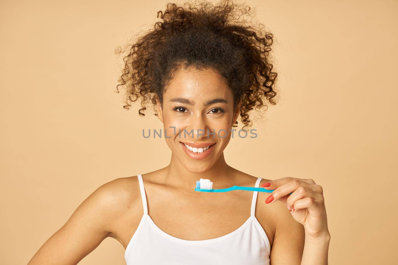 Portrait of cute young mixed race woman brushing teeth in the morning, posing isolated over beige background by friendsstock