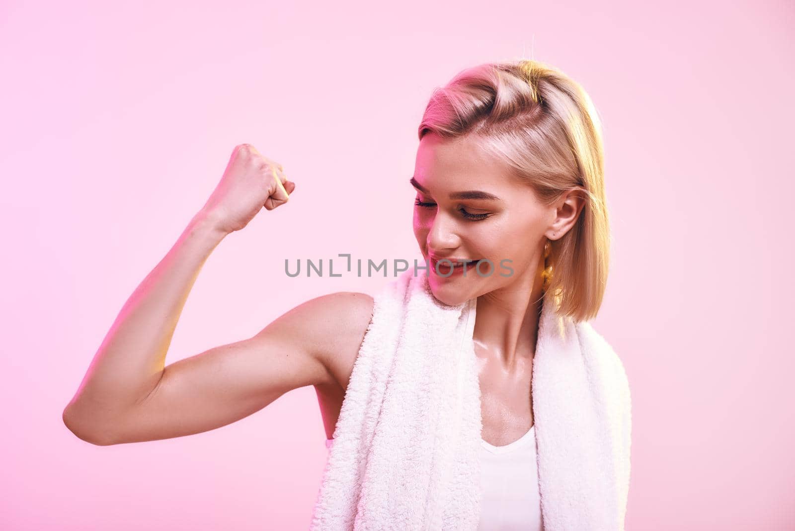 You are stronger than you think Attractive young sporty woman showing her bicep and smiling while standing against pink background. Sport. Active lifestyle. Workout. Human body