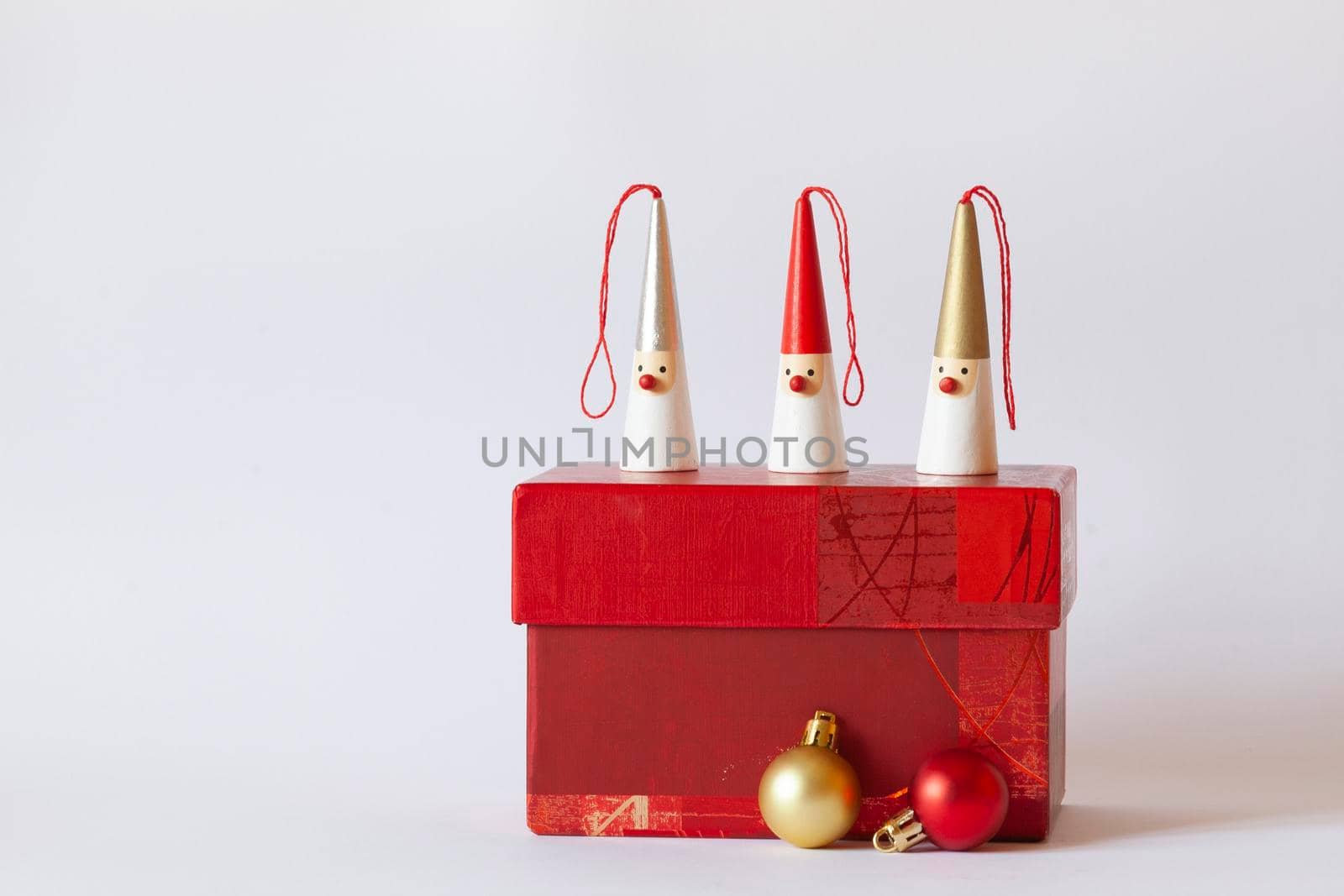 three Santa Clauses figurines on a red gift box, decorative new year tree balls, white background, side view, copy space