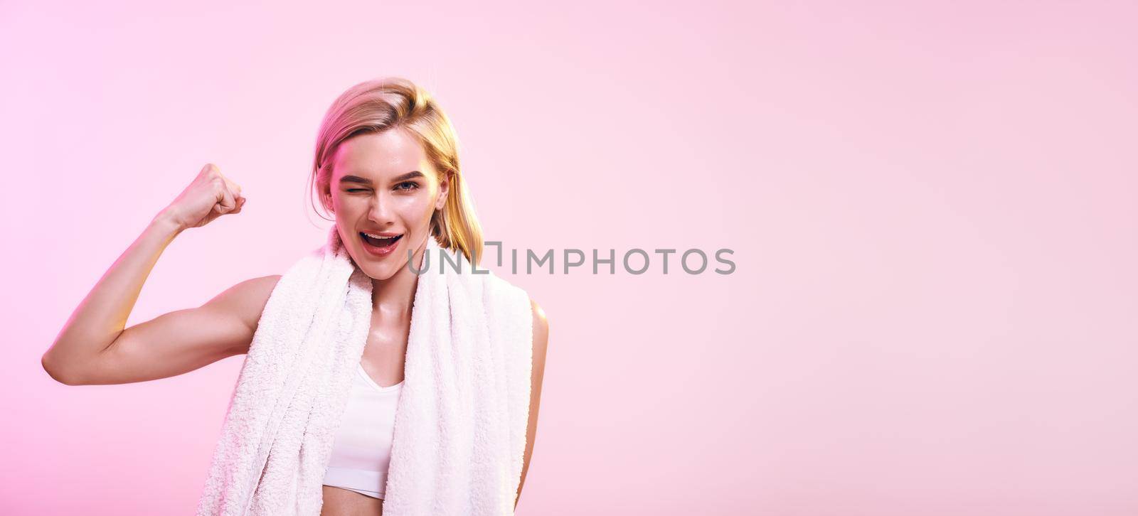 Strength and motivation. Cute and young sporty woman showing her bicep and smiling while standing against pink background. Web banner by friendsstock