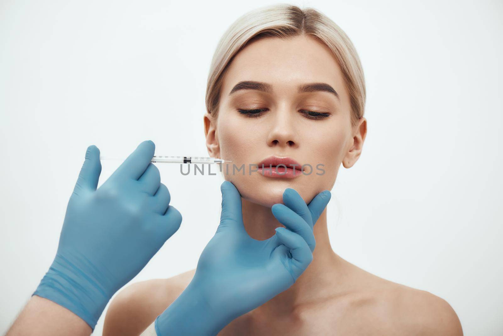 Botox injection. Young attractive woman keeping her eyes closed while doctors hand making an injection in her face. Studio shot. Beauty concept