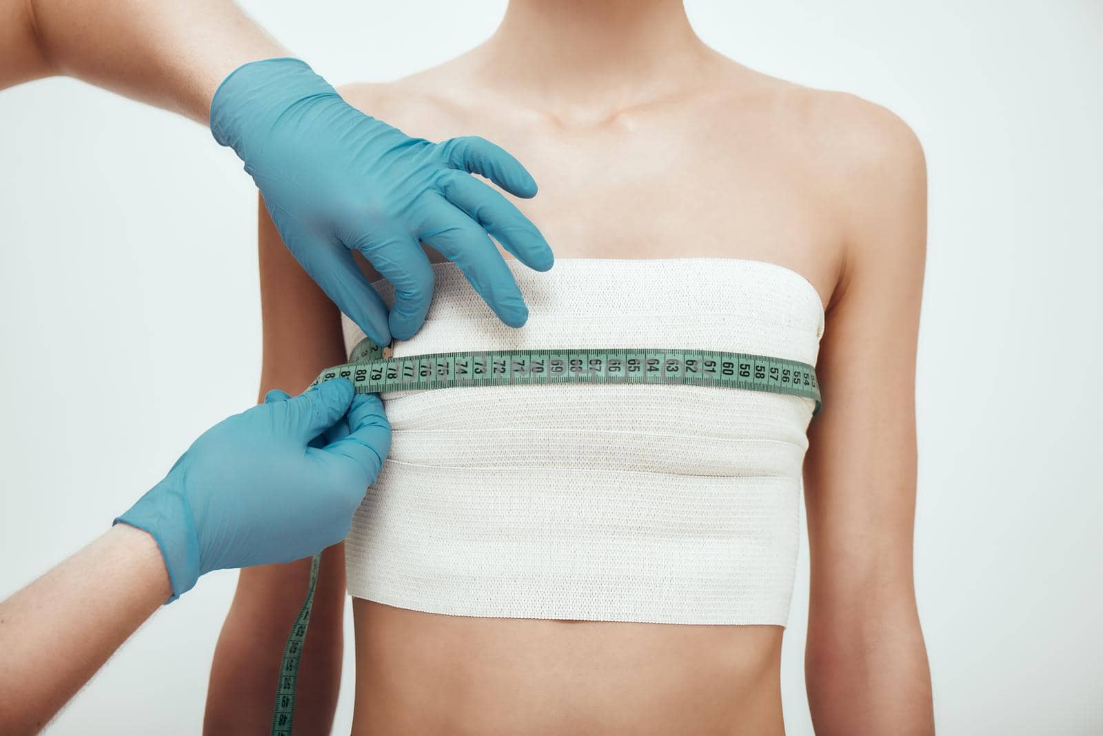 Breast augmentation operation. Cropped photo of woman waiting for plastic surgery while surgeons in blue medical gloves measuring her breast by friendsstock