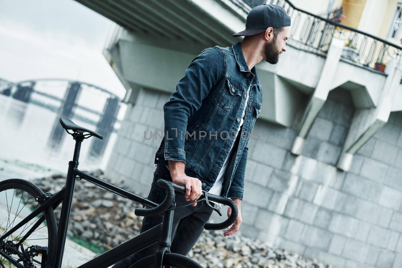 Outdoors leisure. Young stylish man walking on city street with bicycle looking aside pensive by friendsstock