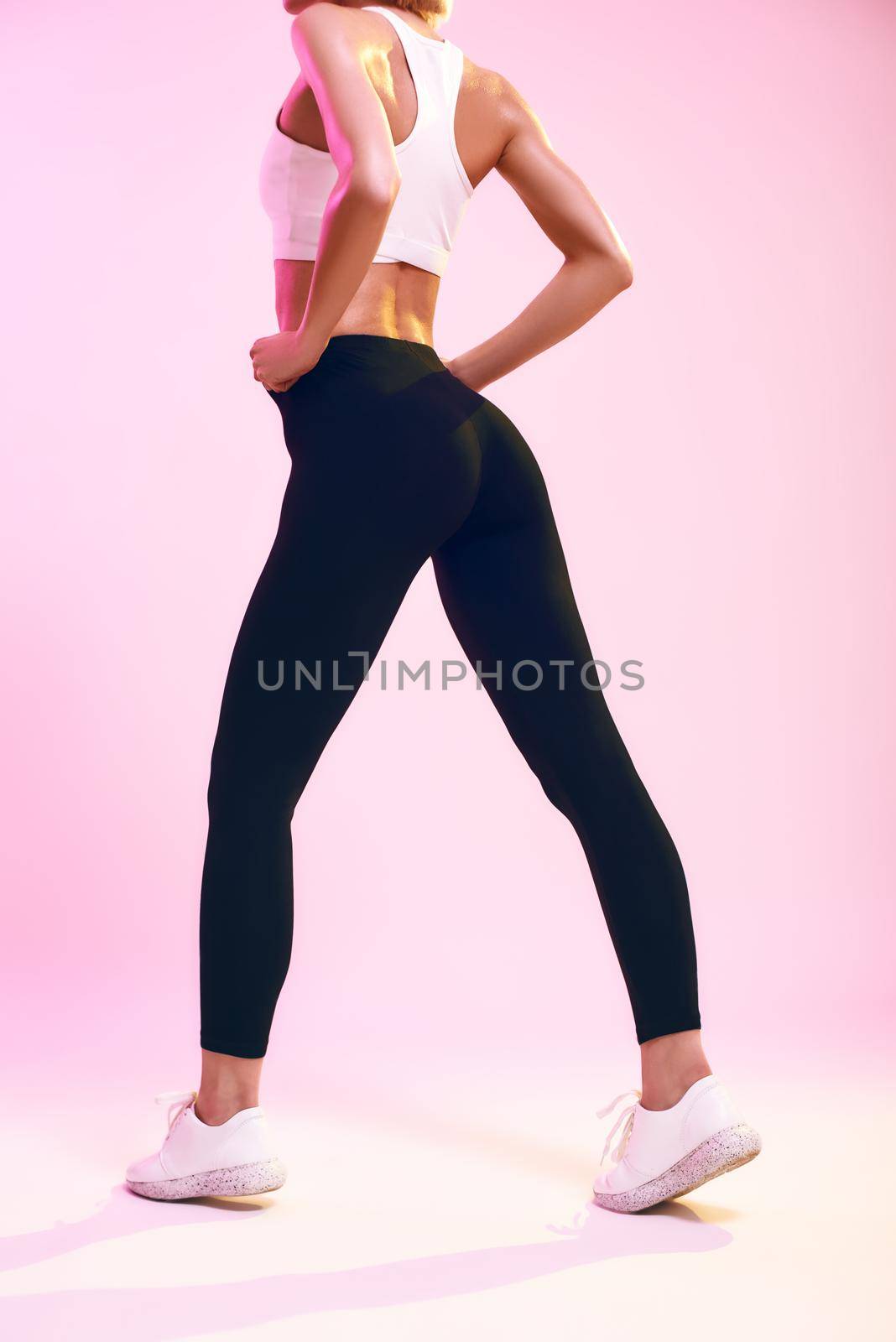 Beautiful buttocks. Back view of sporty slim woman with ideal body in sportswear standing against pink background in studio. Sport. Active lifestyle. Human body