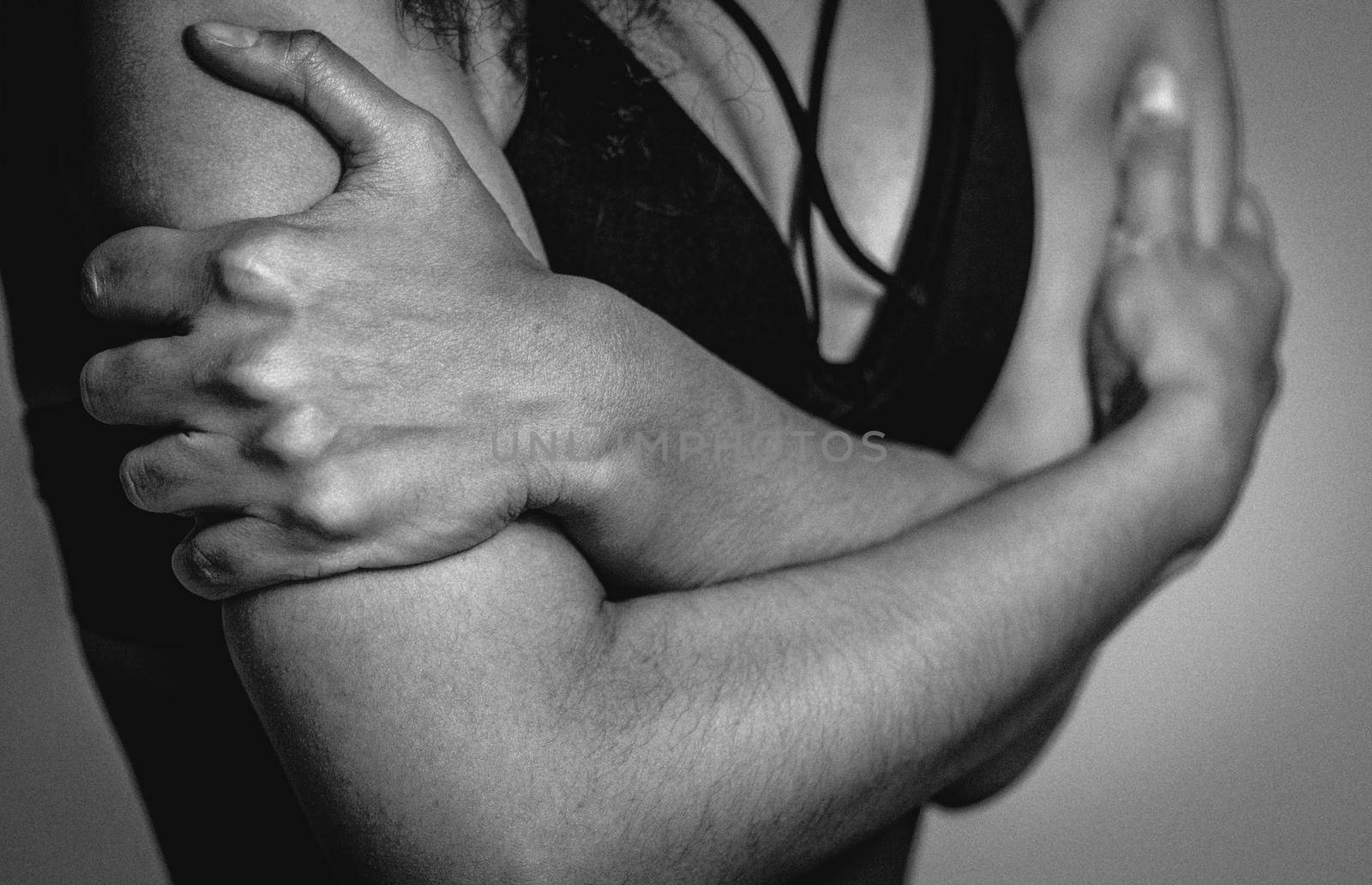 Black and white no face visible. Self-defense, fearful African American girl standing covered with hands in black bare shoulder top isolated on grey background. Human emotions concept.