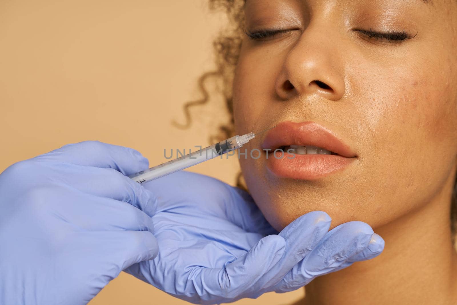 Close up shot of cosmetic injection to the lips of pretty young woman isolated over beige background. Beauty, cosmetology concept. Horizontal shot