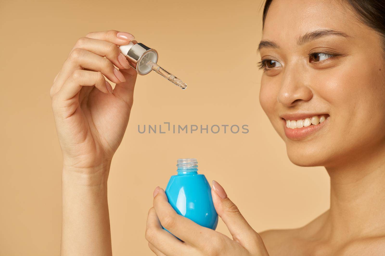 Adorable young woman smiling and holding oil serum with pipette, posing isolated over beige background by friendsstock