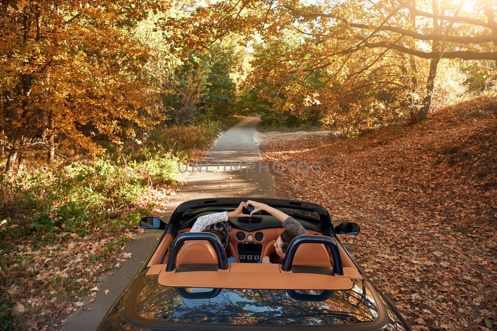 Female friends driving cabriolet with the hands up and having fun on the vacation