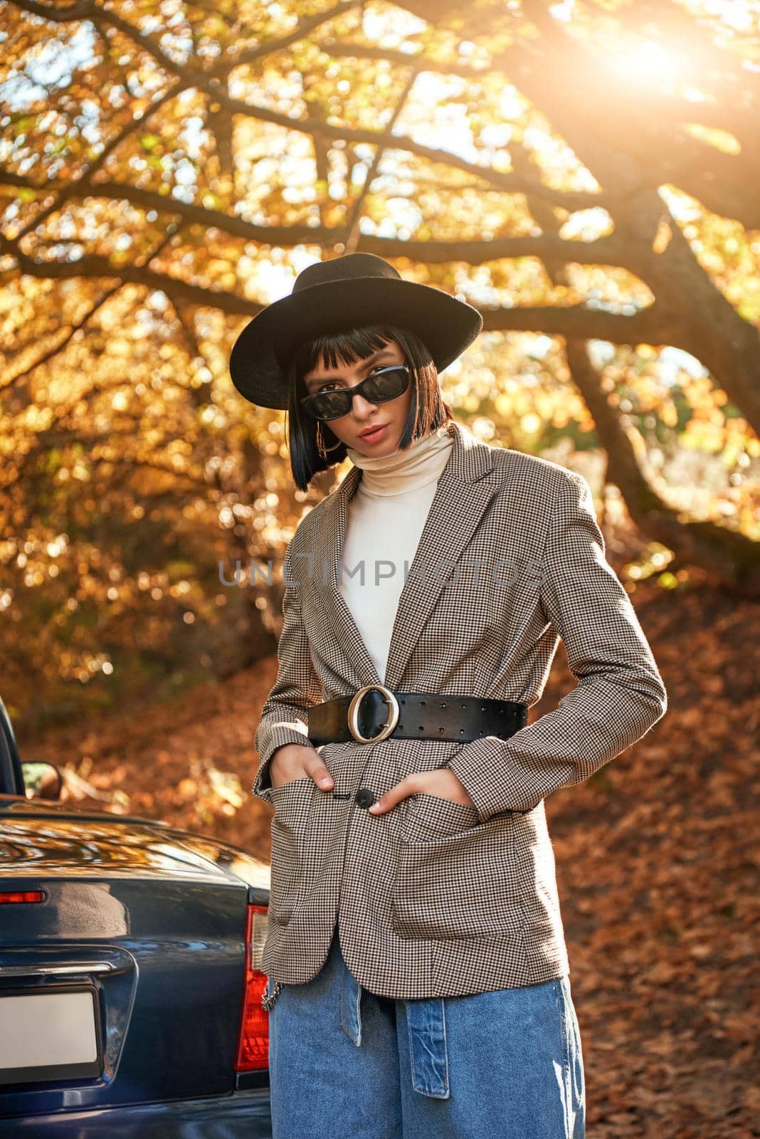 Attractive young woman posing near cabriolet. She wears black hat and sunglasses. Stylish autumn.