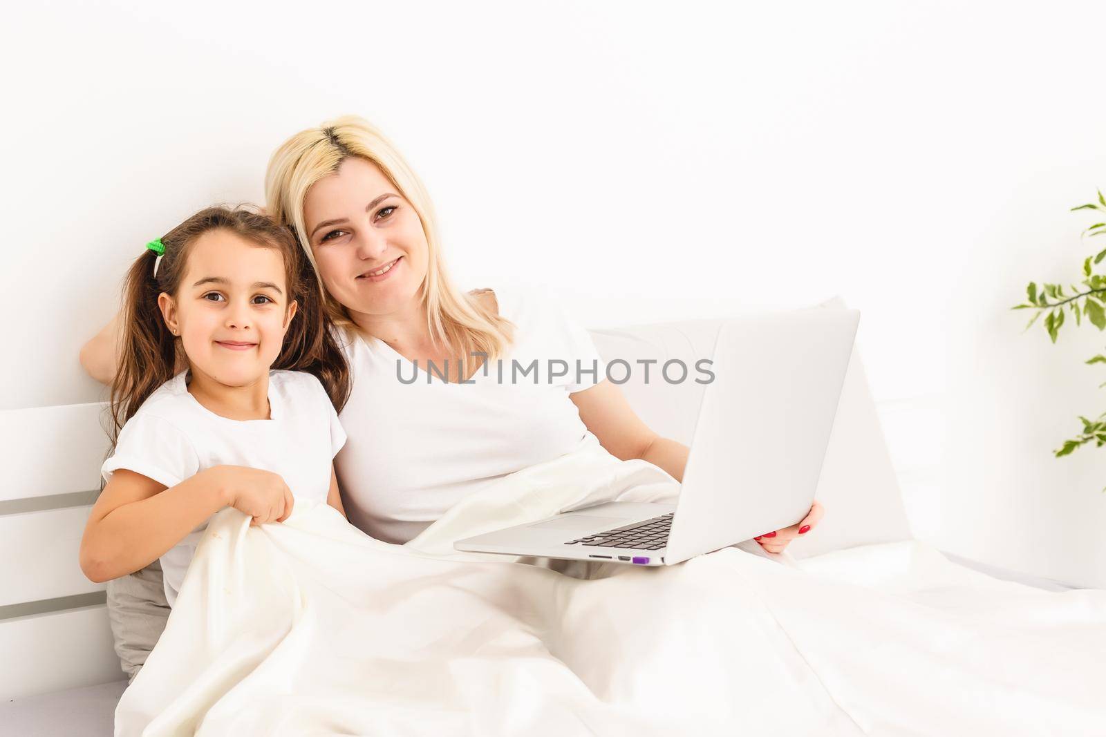 Smiling mother and daughter using laptop in bed at home by Andelov13