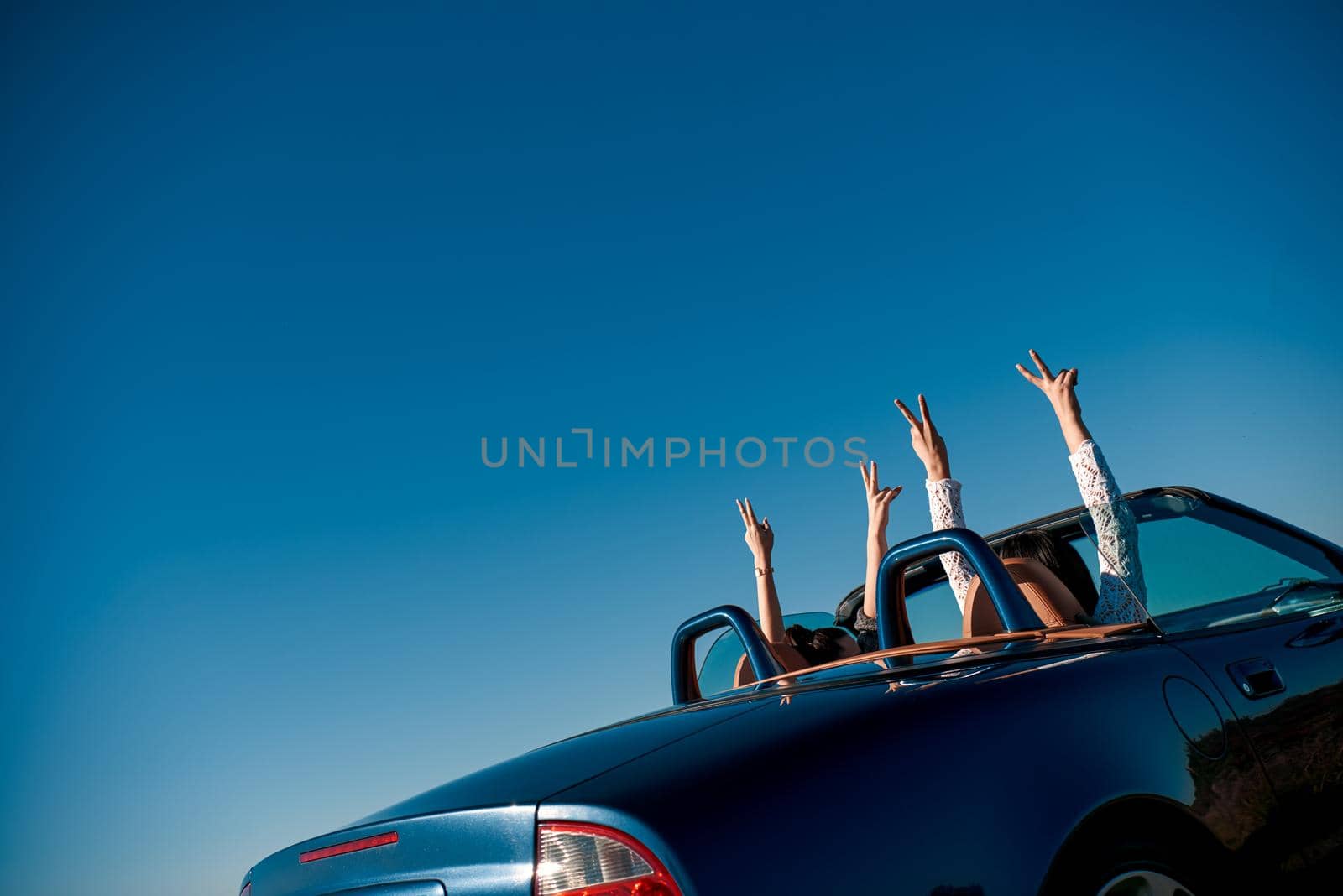 Female friends driving cabriolet with the hands up and having fun on the vacation