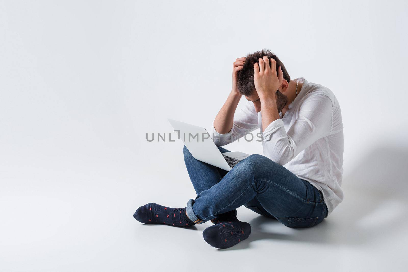 a young man in casual clothes working on a laptop. frustrated his head in his hands