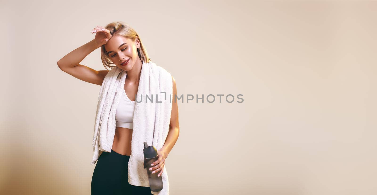 It was great workout Cute and young sporty woman in sports clothing with towel on shoulders keeping eyes closed and smiling while standing in studio. Sport. Active lifestyle