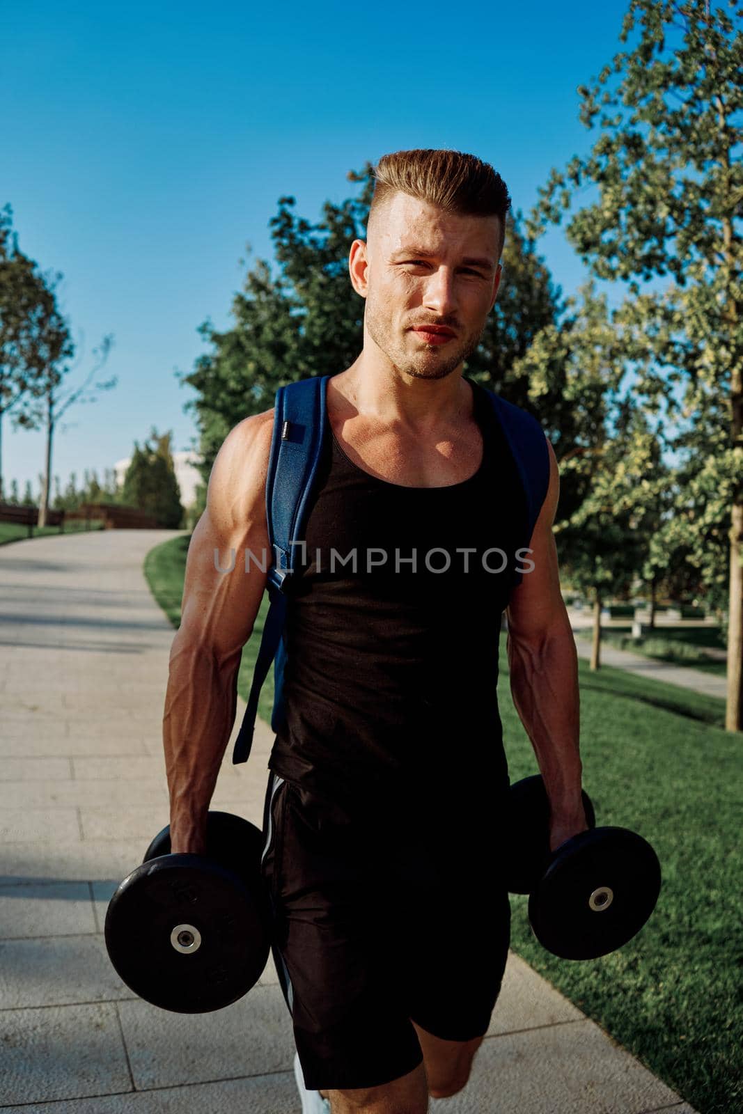 athletic man with dumbbells in his hands in the park training lifestyle by Vichizh