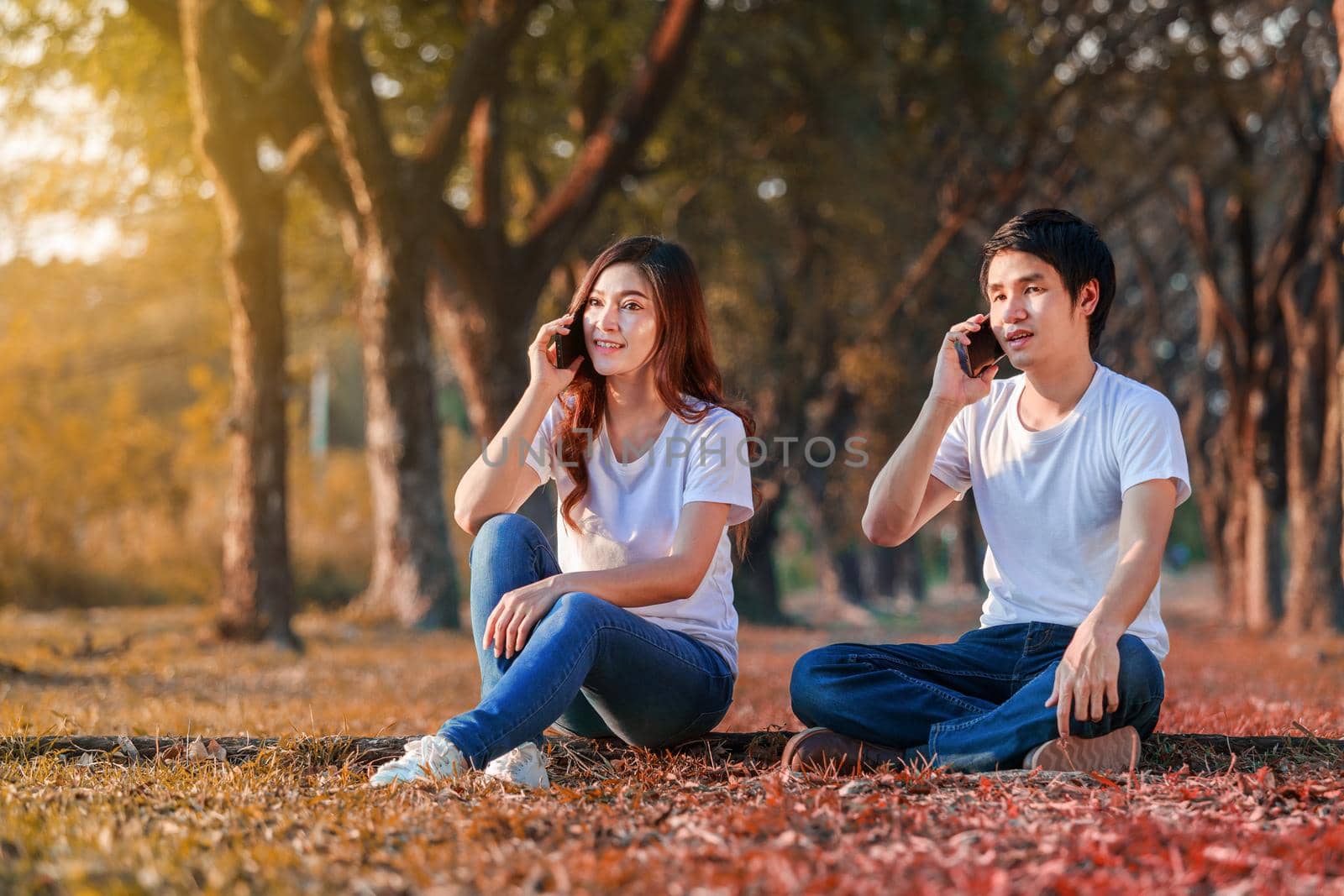 young couple talking on mobile phone in park by geargodz