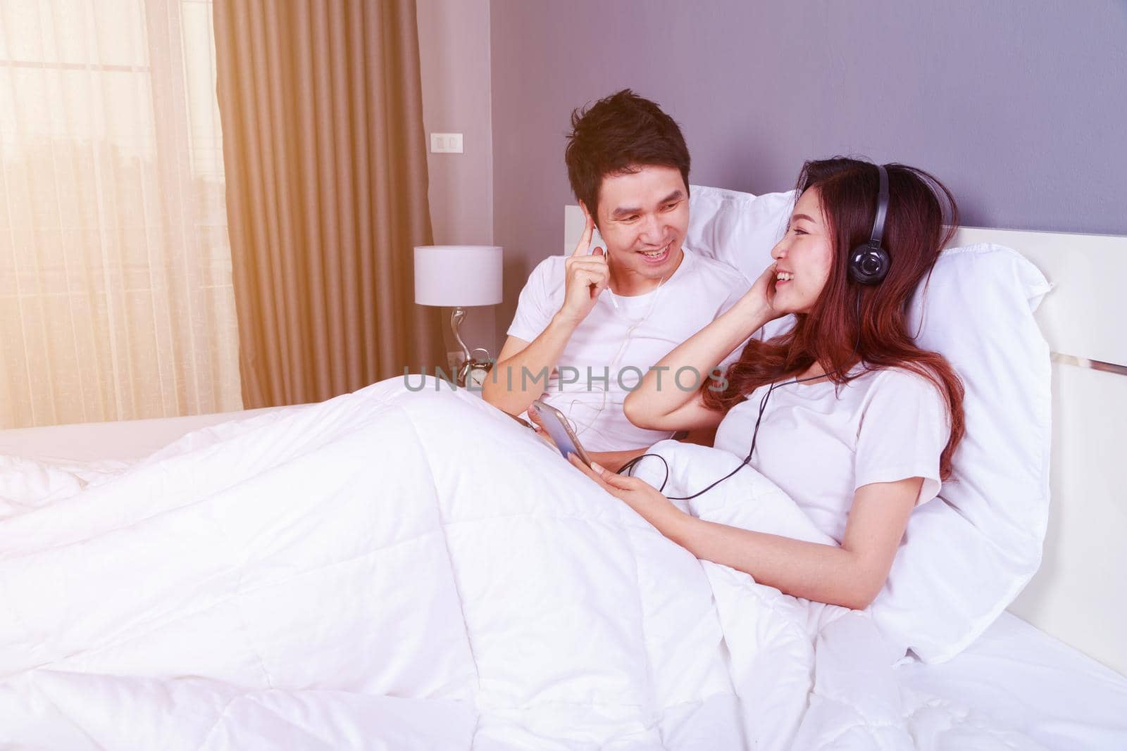 couple listening music from mobile with headphone on bed by geargodz