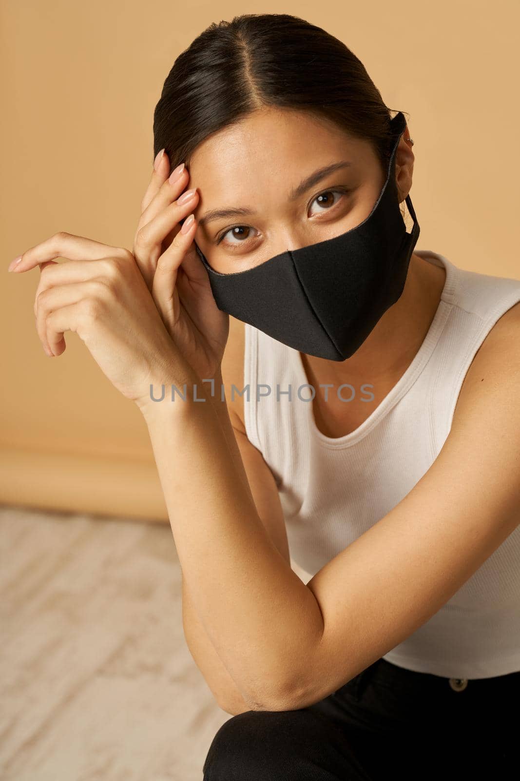 Portrait of adorable young mixed race woman wearing black facial mask, staying safe while posing for camera isolated over beige background. Safety, pandemic concept