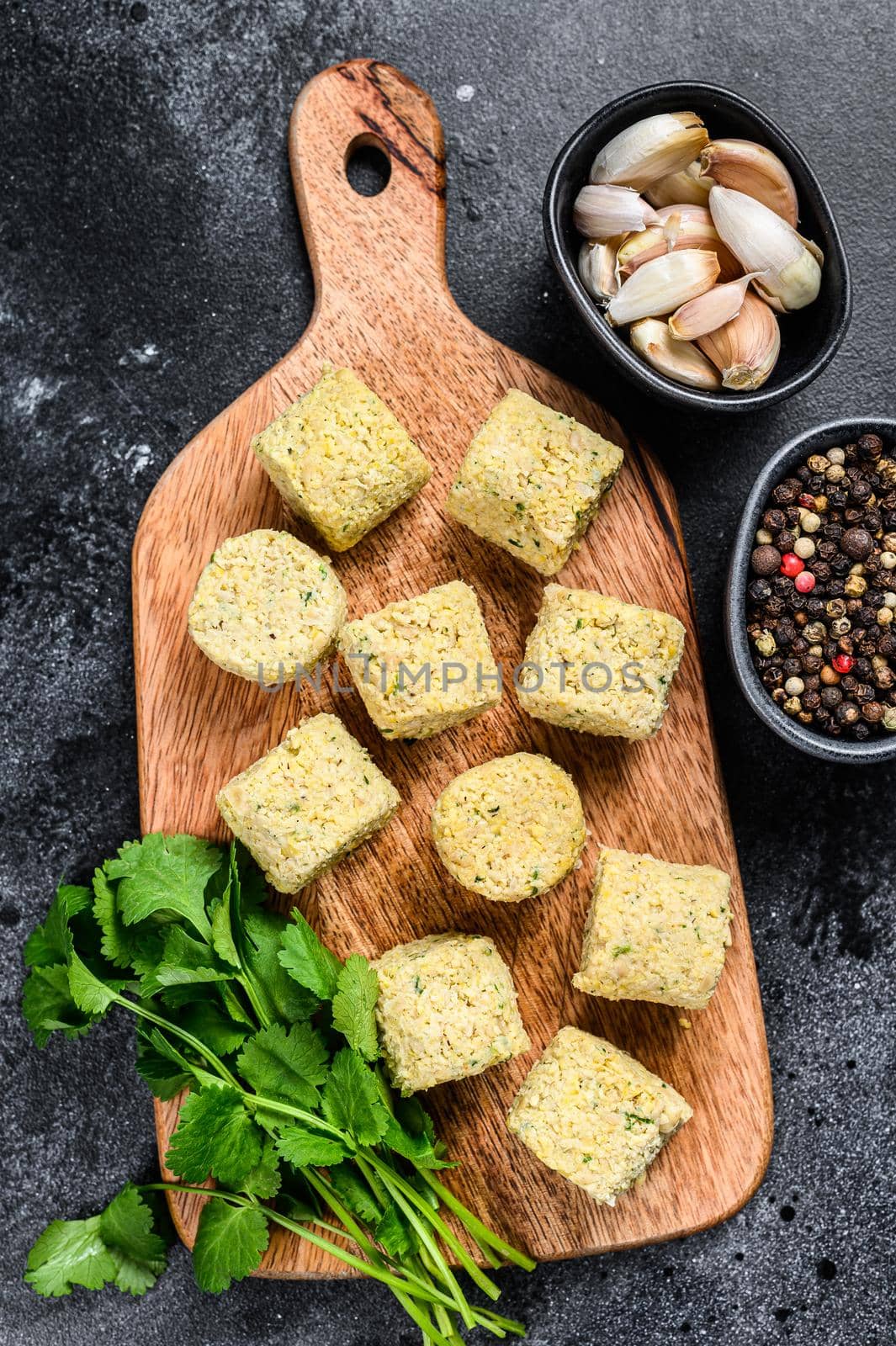 Raw falafel balls on a wooden cutting board. Black background. Top view.