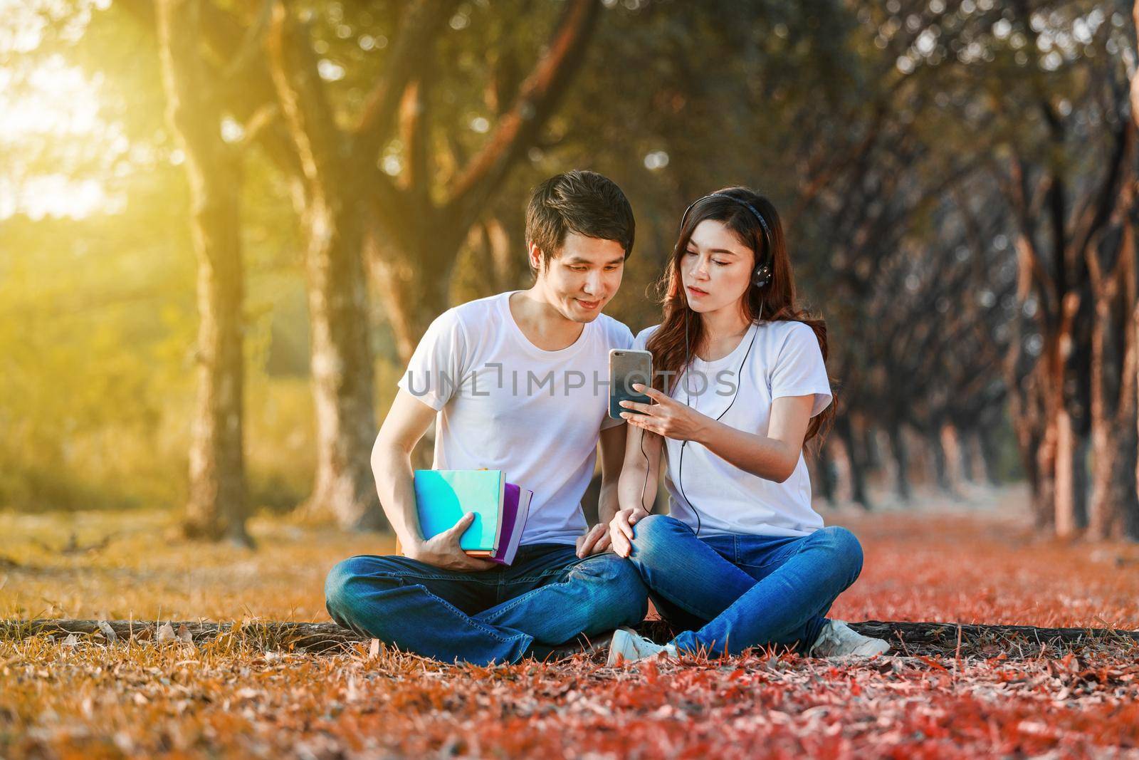 couple listening music from mobile with headphone in the park by geargodz