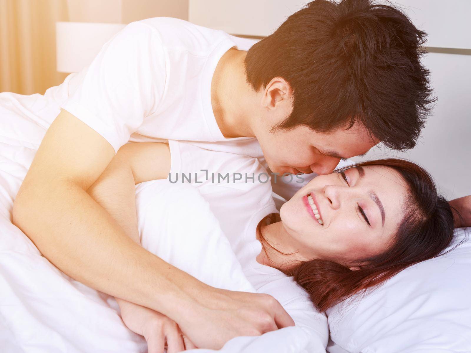 man is kissing his beautiful smiling wife in cheek on bed by geargodz