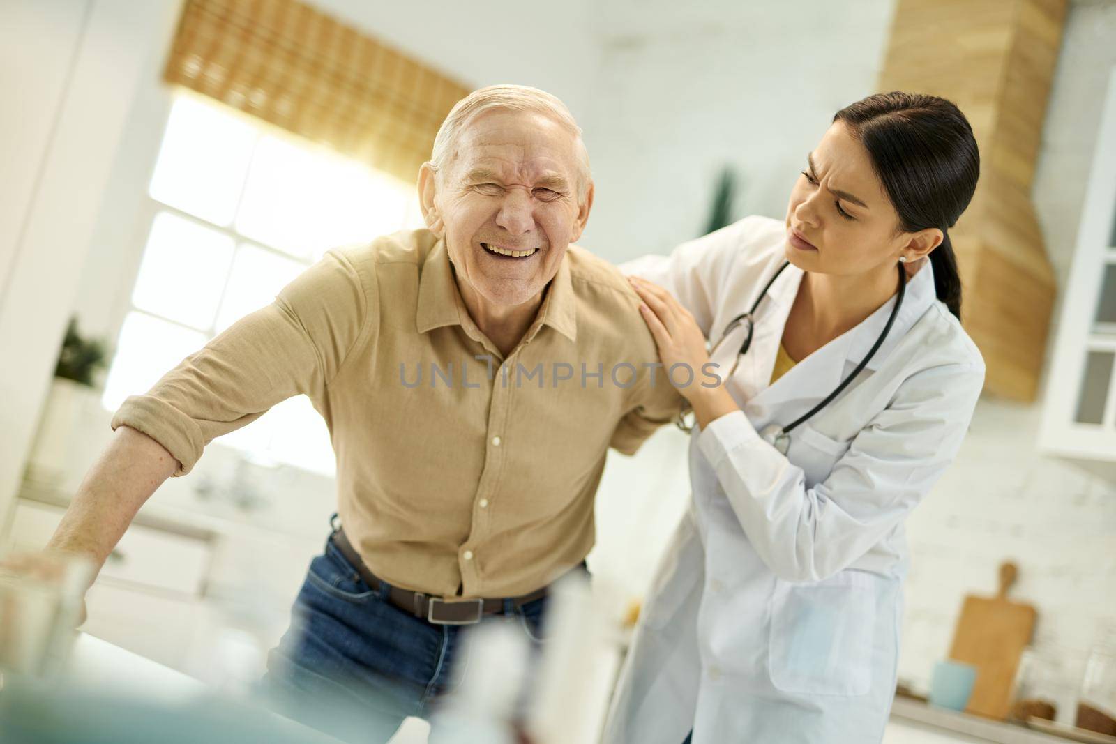 Worried medical worker assisting elderly man with getting up by friendsstock