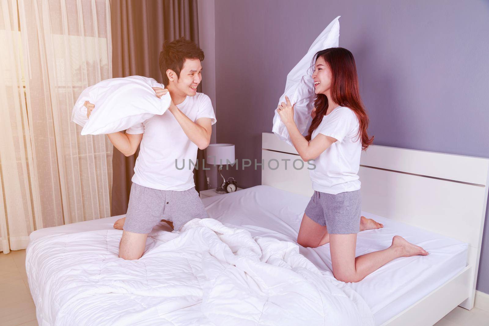 cheerful young couple having a pillow fight on bed in the bedroom