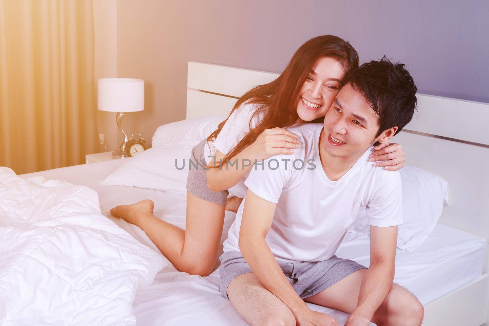 happy young attractive couple hugging on bed in bedroom by geargodz