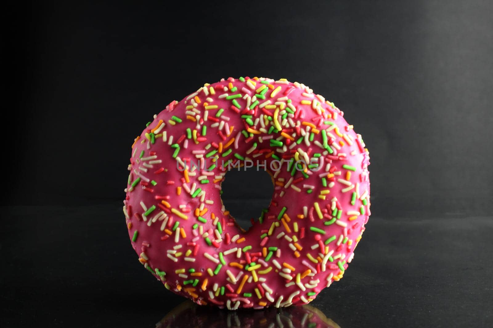 Berliner Donat in pink glaze with colored topping on a black background with a place for text and a copyspace of the delicious food cooking.