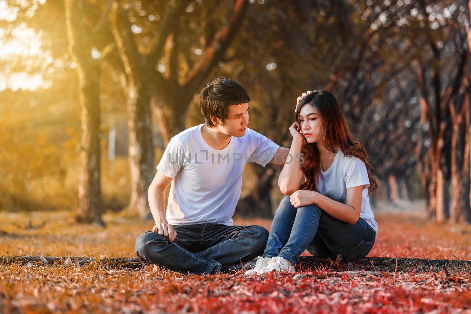 unhappy woman sitting with a concerned guy comforting her in the park