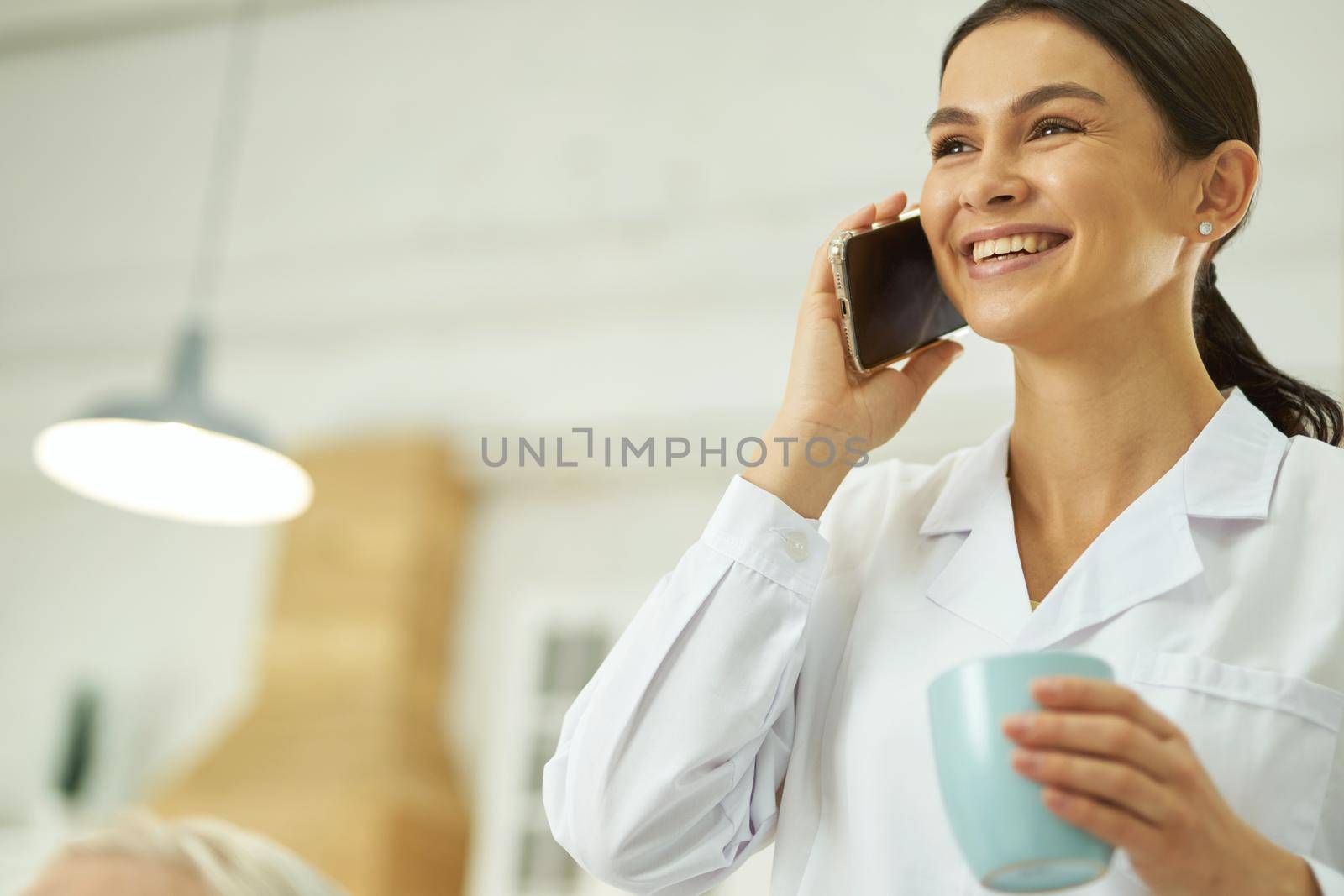 Smiling female doctor using smartphone and drinking hot drink by friendsstock