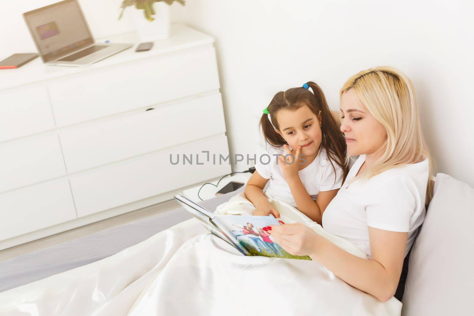 mother and daughter in bed watching a photo book by Andelov13