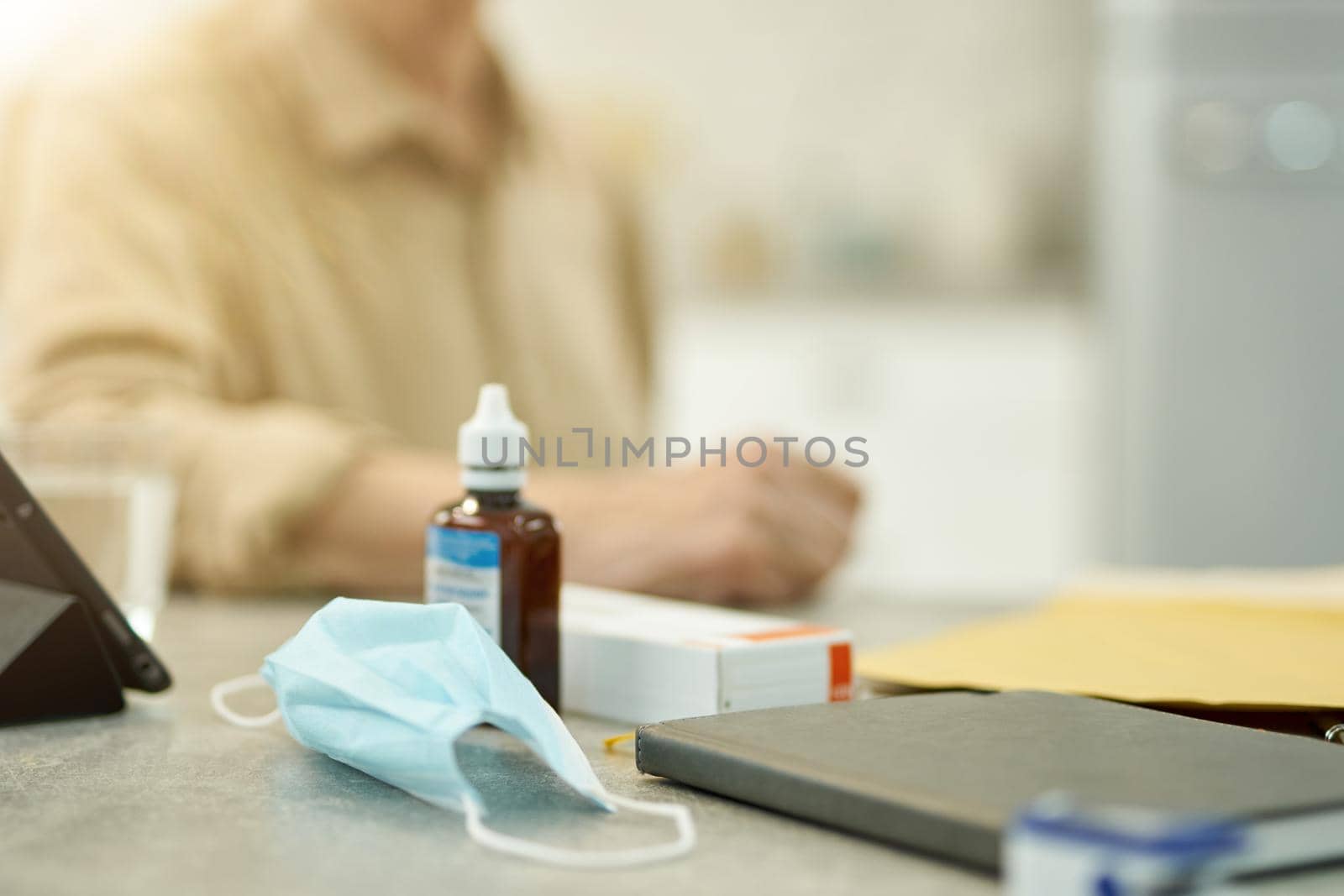 Cropped photo of surgical mask and a bottle of sanitizer sitting on the table of an elderly man