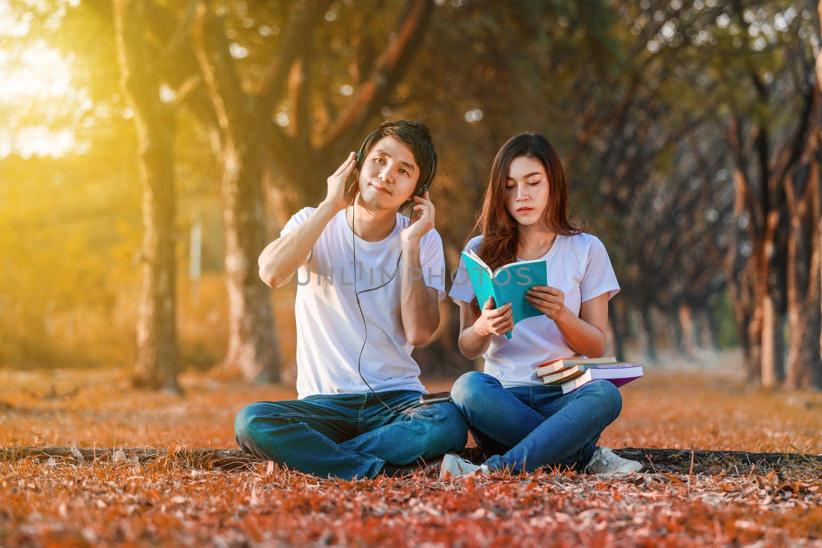 young couple reading a book and listening music with headphone in park by geargodz