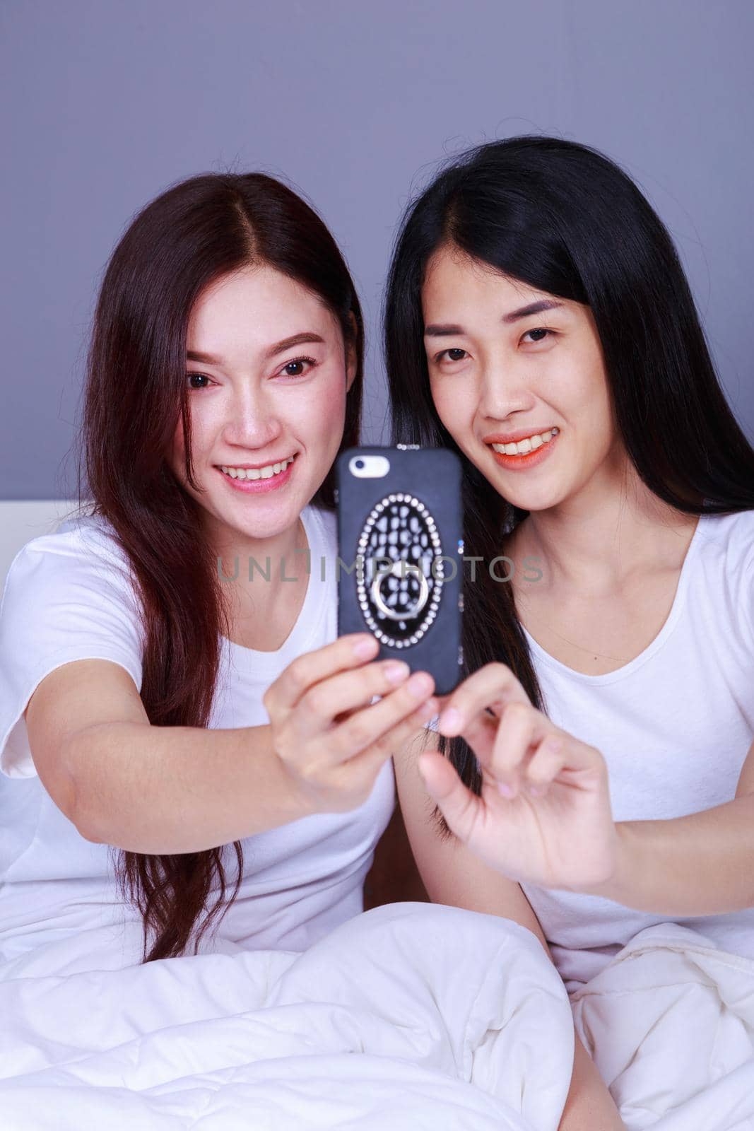 two woman sitting on bed have fun and make selfie by geargodz